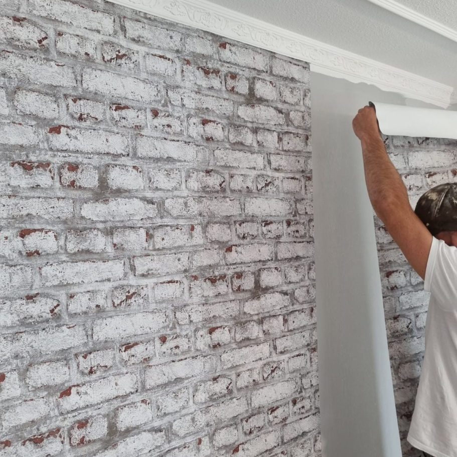 tapezierte Wand Ziegelmuster Mann tapeziert eine Wand mit strukturiertem, weißem Ziegelmuster.